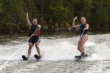 A Father And Daughter Waterskiing Side By Side While Waving To The Camera, Ontario, Canada