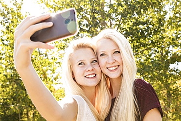 Two Sisters Having Fun Outdoors In A City Park In Autumn And Taking Selfies Of Themselves, Edmonton, Alberta, Canada