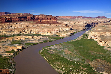 Low Altitude Aerial View Of The Colorado River Winding Through Canyon Country Of Southern Utah, A Bridge Spanning The River In The Background With Red Rock Canyon Walls And Blue Skies, Utah, United States Of America