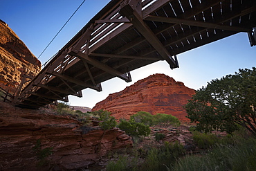 A Footbridge Spanning A Canyon Stream Stretches Overhead With Tall, Red-Rock, Canyon Walls In The Background, Viewed From Under The Bridge, Utah, United States Of America