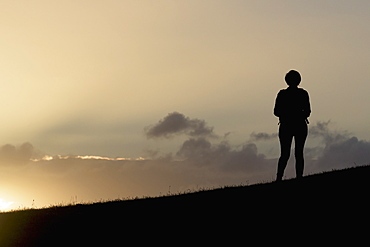 Silhouette Of A Person Standing On A Ridge Overlooking The Sunlight Shining Through The Clouds On Calton Hill, Edinburgh, Scotland