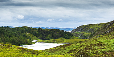 A River Flowing Into A Pond Surrounded By Lush Grass And Forest In The Highlands, Scotland