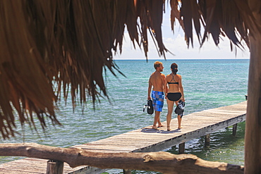 A Couple Walks On A Wooden Dock With Snorkelling Gear, Saint Georges Caye Resort, Belize City, Belize