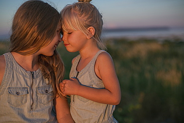 Sisters Sitting Together On The Beach At Sunset, Surrey, British Columbia, Canada