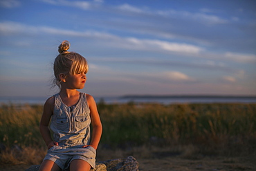 Portrait Of A Young Girl Sitting On A Rock On A Beach At Sunset, Surrey, British Columbia, Canada