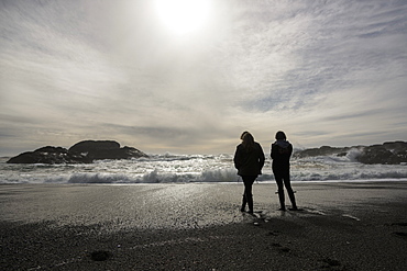 Silhouettes Two Girls Standing At The Water's Edge Looking At The Waves, Vancouver Island, Tofino, British Columbia, Canada