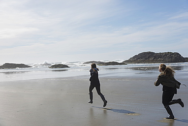 Teenage Girls Running On A Wet Beach At The Coast, Vancouver Island, Tofino, British Columbia, Canada