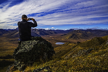 Man Using A Smart Phone To Take Photos On A Look Out Overlooking The Blackstone Valley, Along Dempster Highway, Yukon, Canada