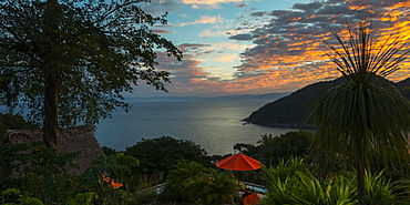 Glowing Golden Clouds At Sunset Over The Pacific Ocean And A Silhouetted Coastline And A Red Umbrella At A Resort On The Shore, Jalisco, Mexico