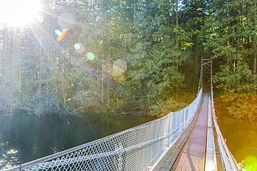 Sunshine lights the way along a suspension bridge across the end of Buntzen Lake trail to continue the path into the forest trails near Vancouver, British Columbia, Canada