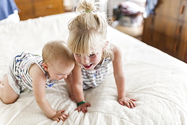 Two sisters, a baby and a toddler, play together on a bed, Sorrento, British Columbia, Canada