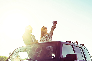 Young couple taking self-portraits with a cell phone while standing up in their sunroof of their vehicle, Edmonton, Alberta, Canada