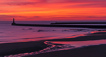 Silhouette of a pier and lighthouse with dramatic and vibrant sunrise colours in the sky and reflected in the ocean water, Sunderland, Tyne and Wear, England