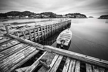 Black and white image of a boat tied to a wooden dock in a harbour along the Atlantic coast, Newfoundland, Canada