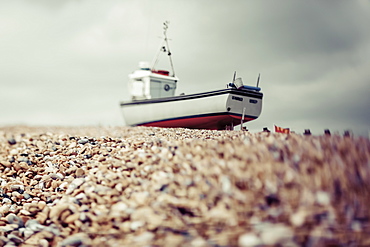 A fishing boat sits on the rocky beach under a cloudy sky, Hastings, England