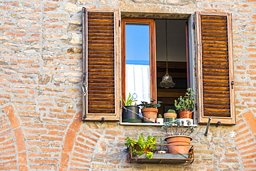 Close View Of A Montepulciano Brick House Facade With Opened Window, Flowerpots And Latticed Sun Blinds, Tuscany, Italy