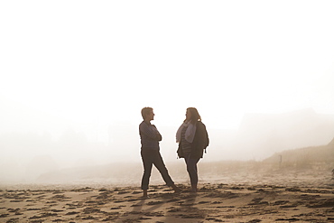 Two Female Friends Stand Talking On A Beach In The Mist, Prince Edward Island, Canada