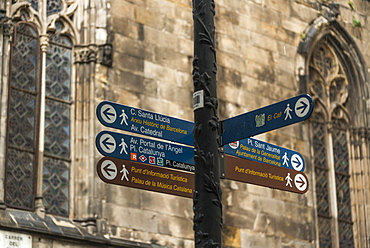 Destination Signs For Landmarks On A Post With An Old Stone Wall And Windows In The Background, Gothic Quarter, Barcelona, Catalonia, Spain