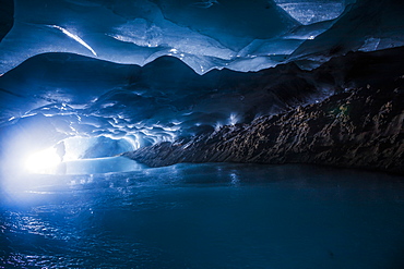 A Man Is Silhouetted By The Entrance To A Dark Ice Cave Within Augustana Glacier In The Alaska Range, Alaska, United States Of America