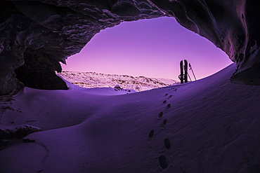 Footprints Lead Toward A Splitboard Placed At The Entrance Of An Ice Cave Within Canwell Glacier In The Alaska Range After Sunset In Winter, Alaska, United States Of America