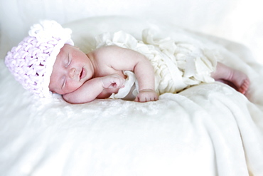 A Newborn Baby Lays Sleeping On A White Blanket Wearing A Pink Knit Hat, Washington, United States Of America