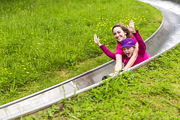 Two Smiling Teenage Girls Slide Down A Bobsled Track Embracing Each Other, Arms Raised In Joy, North Rhein, Westphalia, Germany