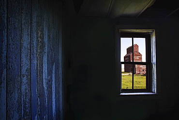 A Grain Elevator Seen Through The Window Of An Old, Abandoned Ghost Town Store; Bents, Saskatchewan, Canada