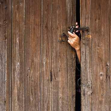 A hand reaching out a wooden door to unlock a padlock