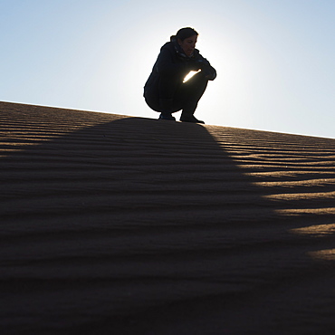 A woman crouching on the top of a sand dune, Souss-massa-draa morocco