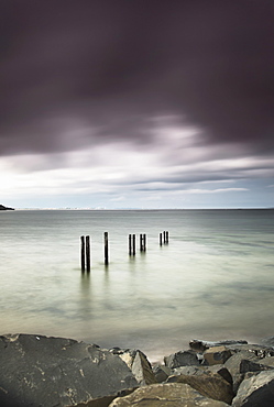 Wooden posts in a row in the shallow water along the coast under dark storm clouds, St. mary's bay northumberland england