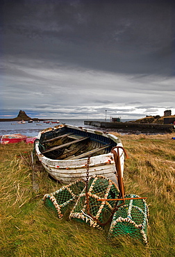 A Weathered Boat And Fishing Equipment Sitting On The Shore With Lindisfarne Castle In The Distance, Lindisfarne, Northumberland, England