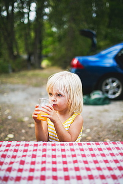 A Young Girl Sits At A Picnic Table Drinking, Peachland, British Columbia, Canada