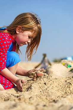 Young Girl Covering Up Persons Feet Lying On A Sandy Beach, Dubai, United Arab Emirates