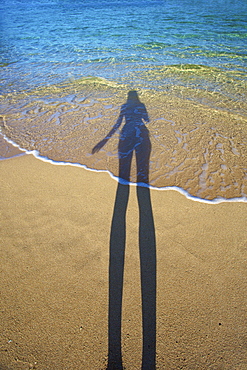 Shadow Of A Woman Standing On The Beach At The Water's Edge, Kauai, Hawaii, United States Of America