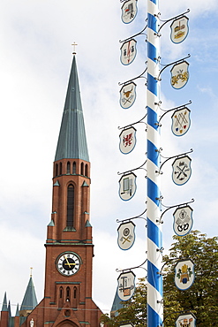 Close Up Of A Traditional Bavarian May Pole With Blue And White Stripes With Crests And A Church Steeple In The Background, Munich, Germany