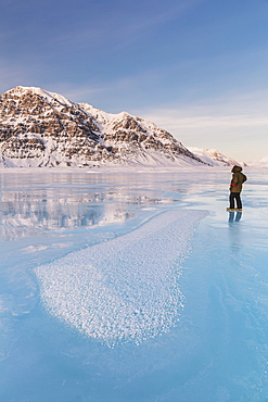 Man In A Parka Standing On Overflow Ice On The Frozen Anaktuvuk River, Hoar Frost Crystals In The Foreground, Napaktualuit Mountain In The Background, Gates Of The Arctic National Park, Alaska, United States Of America