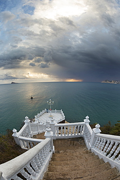 Steps Leading Down To The Turquoise Water With The Sun Glowing On The Horizon Under Storm Clouds, Benidorm, Spain