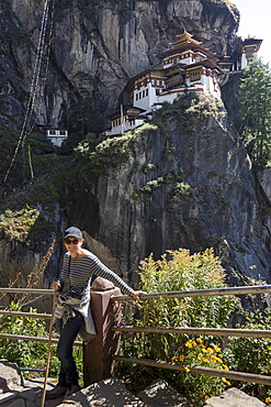 A Woman Stands At A Railing With Taktsang Palphug Monastery In The Background, Paro, Bhutan