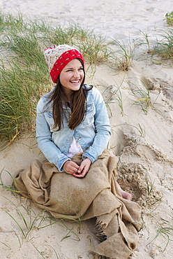 A Young Woman Sits On A Beach Wearing A Knit Hat, Tarifa, Cadiz, Andalusia, Spain