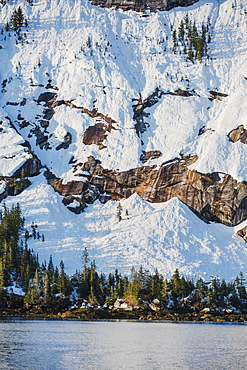 Snow Covered Cliffs And Evergreen Trees Bathed In Sunset Light On The Shore Of Kings Bay, Prince William Sound, Whittier, Alaska, United States Of America