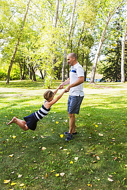 A Father Swinging His Daughter Around In A Park During A Family Outing, Edmonton, Alberta, Canada