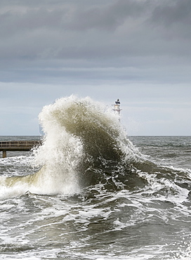 Large Wave Crashing At The Coast With A Lighthouse At The End Of A Pier, Amble, Northumberland, England