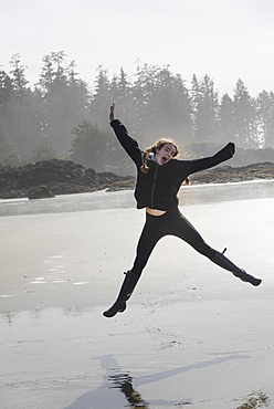 A Girl Leaping In Mid-Air On A Wet Beach, Tofino, British Columbia, Canada