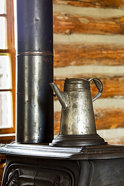 Close Up Of An Old Metal Coffee Pot On Top Of An Old Cast Iron Stove In Log Cabin With Window In The Background, South Of Maple Creek, Alberta, Canada