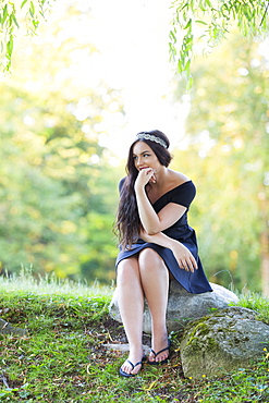 A Young Millennial Teenage Girl Poses For Her Grad Portraits In A Park With A Sparkling Headband And Modest Black Dress, Sitting On A Rock In The Forest Looking Thoughtful, Vancouver, British Columbia, Canada