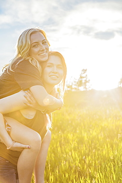 Two friends walking in a park, one giving the other a piggy back ride and posing for the camera, Edmonton, Alberta, Canada