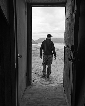 A man and the Valley of Ten Thousand Smokes is framed by the doorway of one of the Baked Mountain Huts in Katmai National Park, Alaska, United States of America