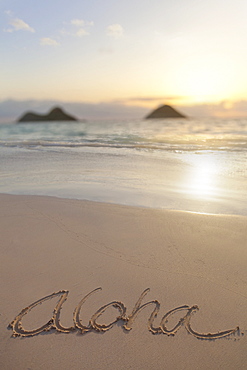 Aloha Written On The Sand On Lanikai Beach In Kailua With Mokulua Twin Islands In The Background At Sunrise, Honolulu, Oahu, Hawaii, United States Of America