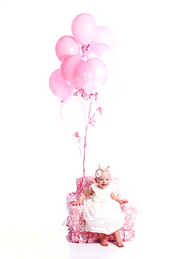 Portrait Of A Young Girl In A White Dress Sitting In A Pink Chair With A Bouquet Of Pink Balloons, Oregon, United States Of America