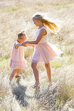 Two Young Girls Dancing In A Field Of Long Grass, Washington, United States Of America